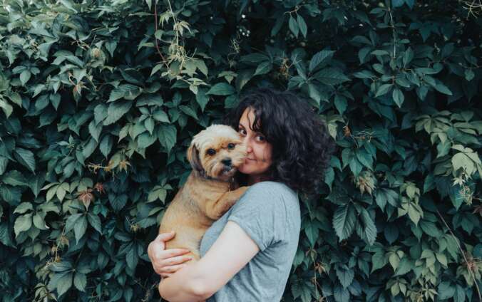 A woman cuddles her golden pup near a green hedge