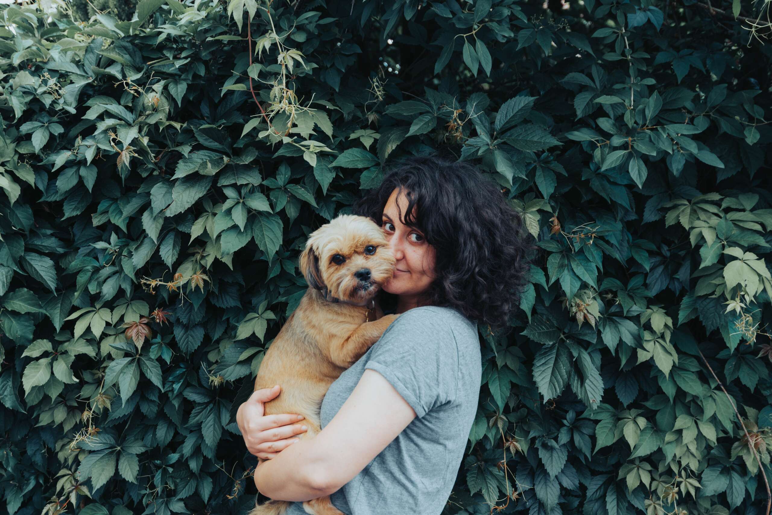 A woman cuddles her golden pup near a green hedge